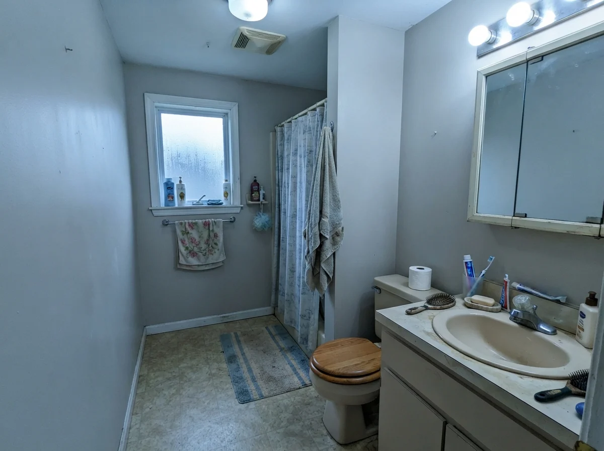 Dated bathroom showing cool light on beige walls with an older beige vanity and toilet.