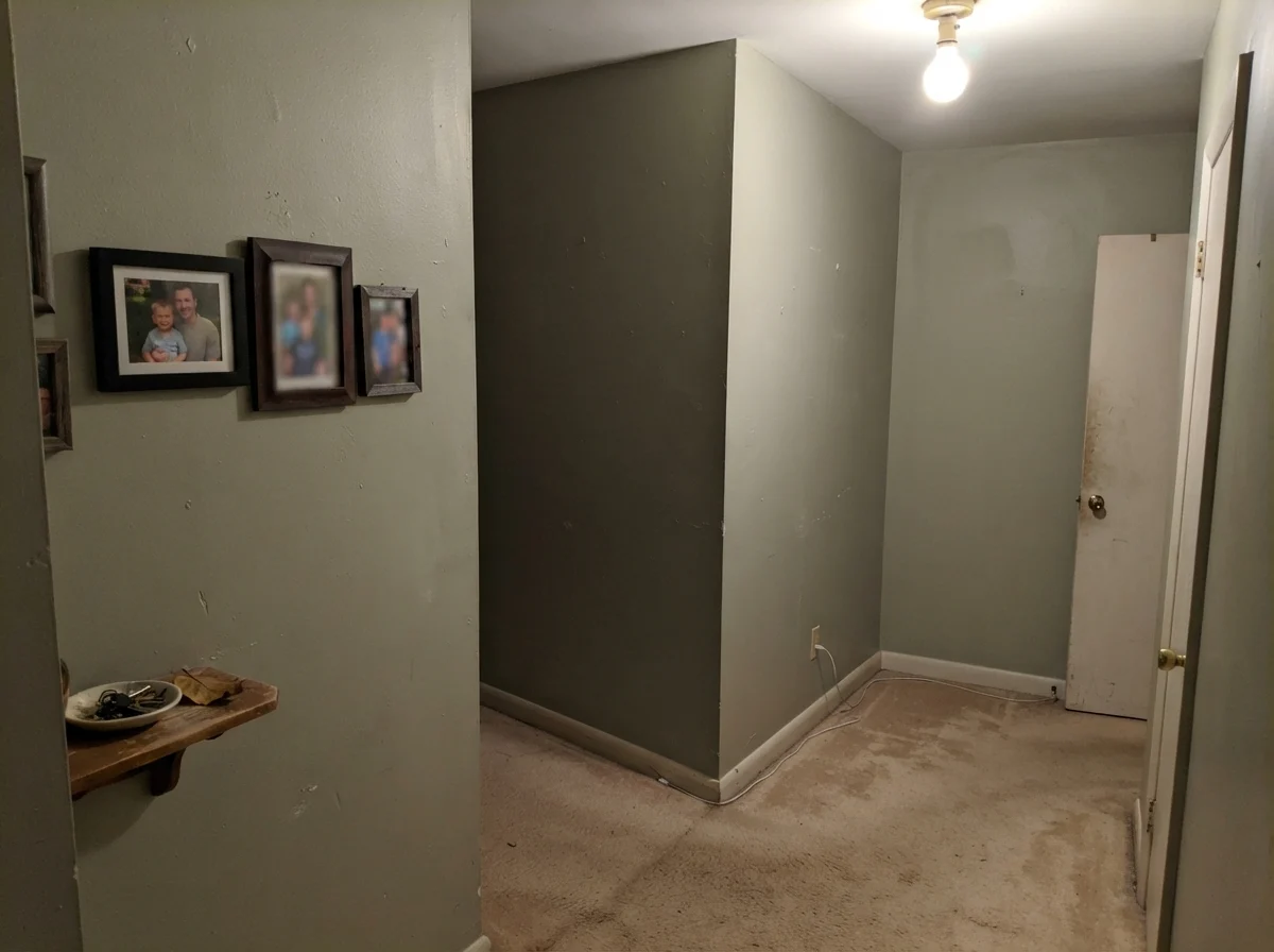 Windowless hallway corner showing muddy, flat October Mist paint under a single bulb