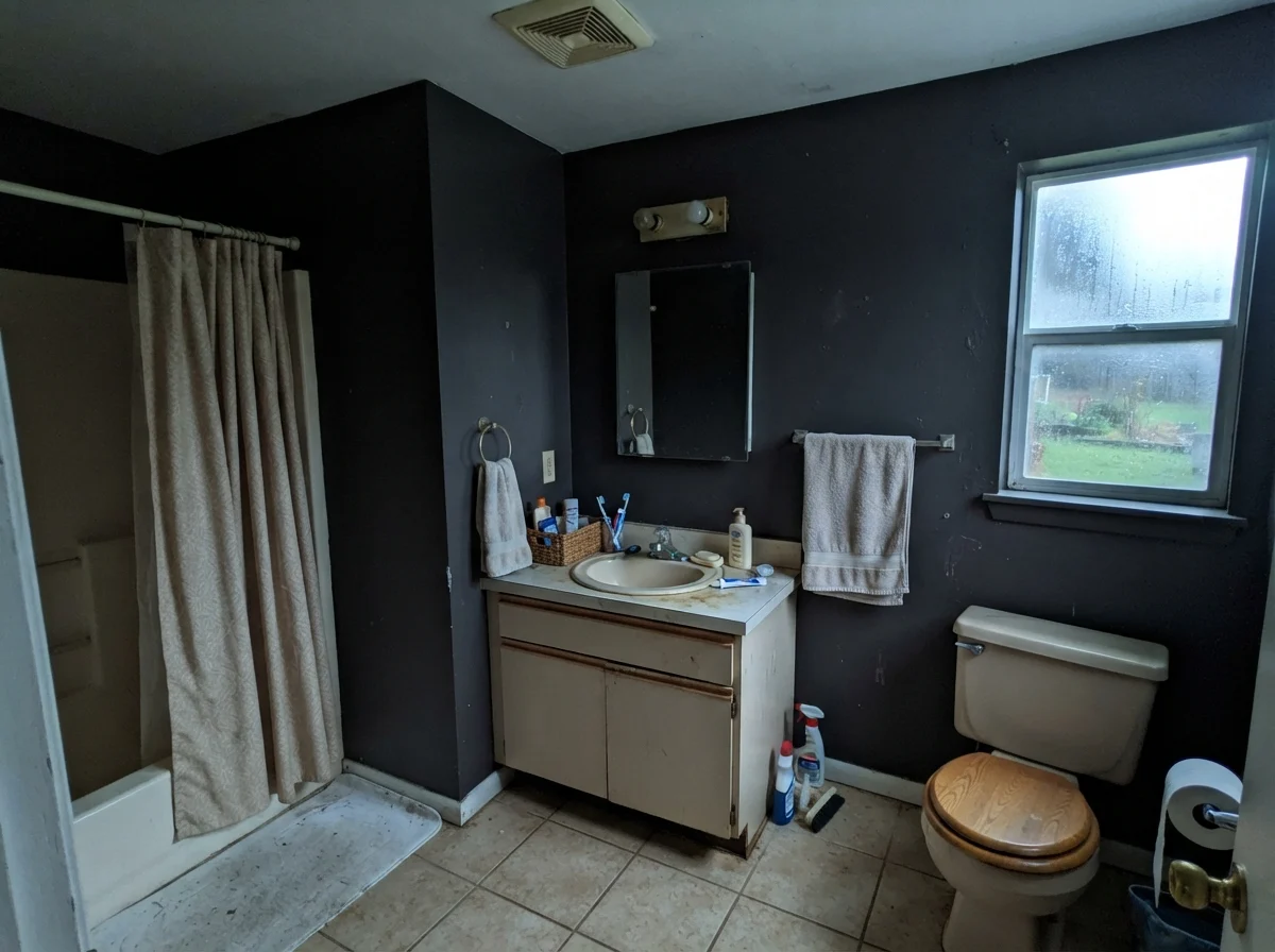 Dated bathroom showing cool tones on walls next to beige vanity on a rainy day.