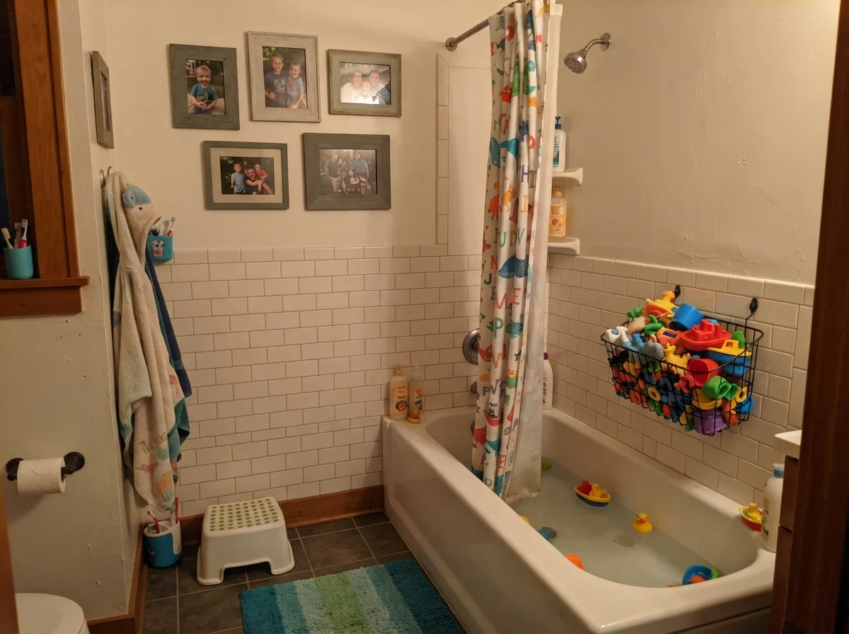 Kids bathroom with wire basket of bath toys, shower curtain, and family photos.